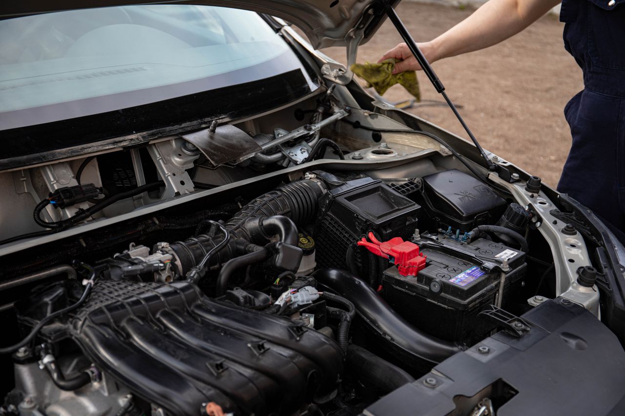 our-story-02 Mechanic inspecting car engine bay and battery during routine maintenance.